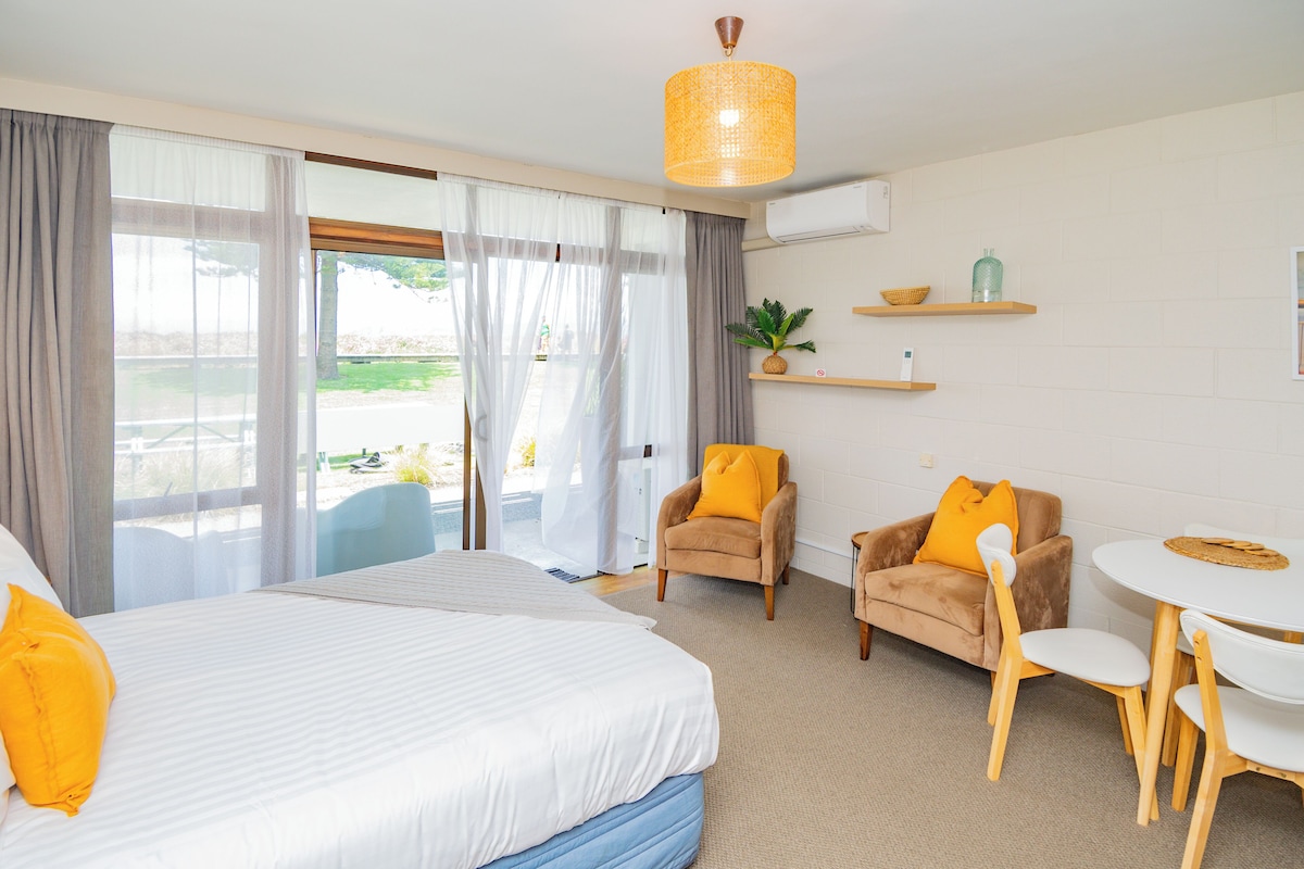 Ein Hotelzimmer mit einem großen Bett, einem Esstisch mit Stühlen, einer kleinen Couch und einem Balkon mit Blick.