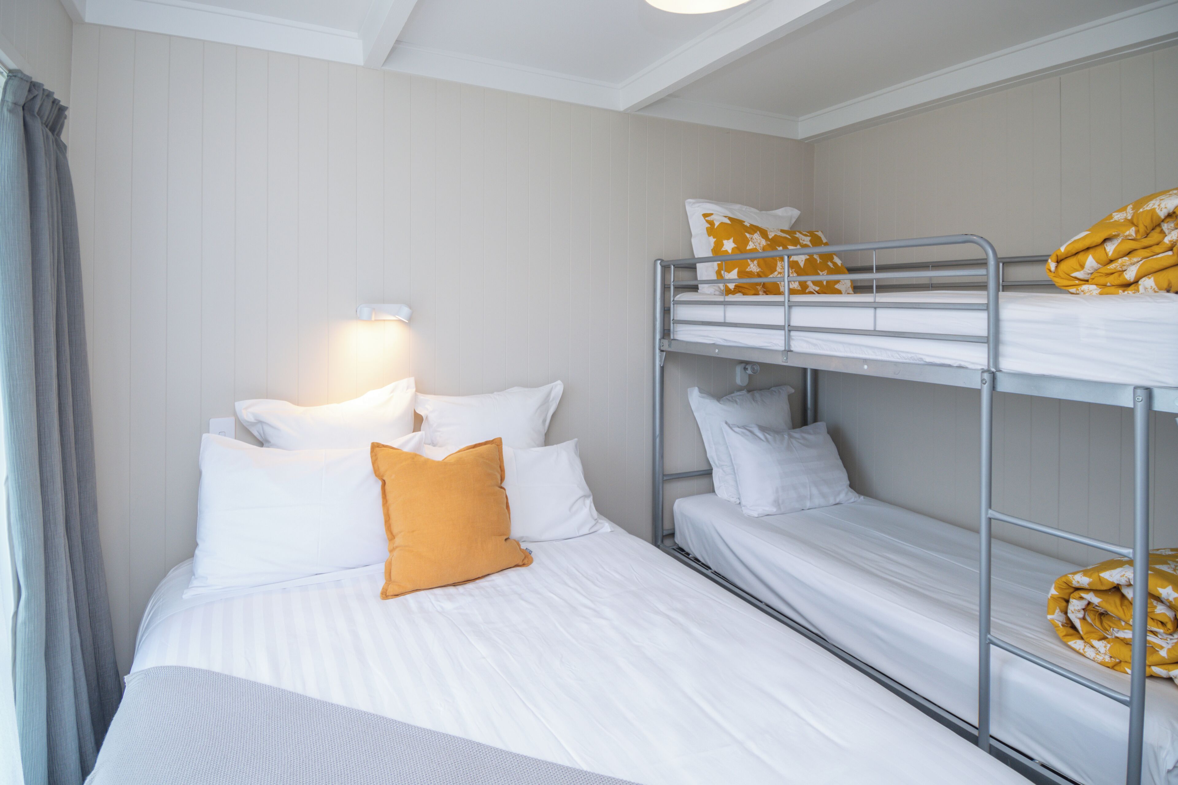 A hotel room with a single bed, a bunk bed, and a bedside lamp.