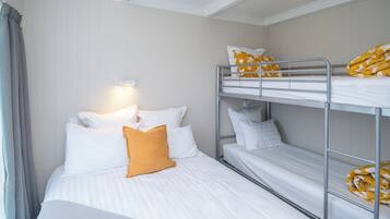 A hotel room with a single bed, a bunk bed, and a bedside lamp.