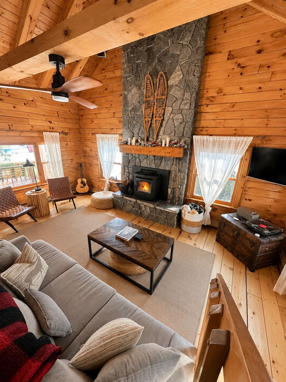 A cozy cabin interior with a stone fireplace, wooden walls, a sofa, a coffee table, and a television.