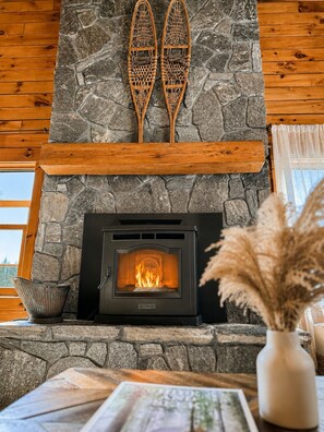 A stone fireplace with a visible fire, a wooden mantel, and a pair of skis mounted above it.