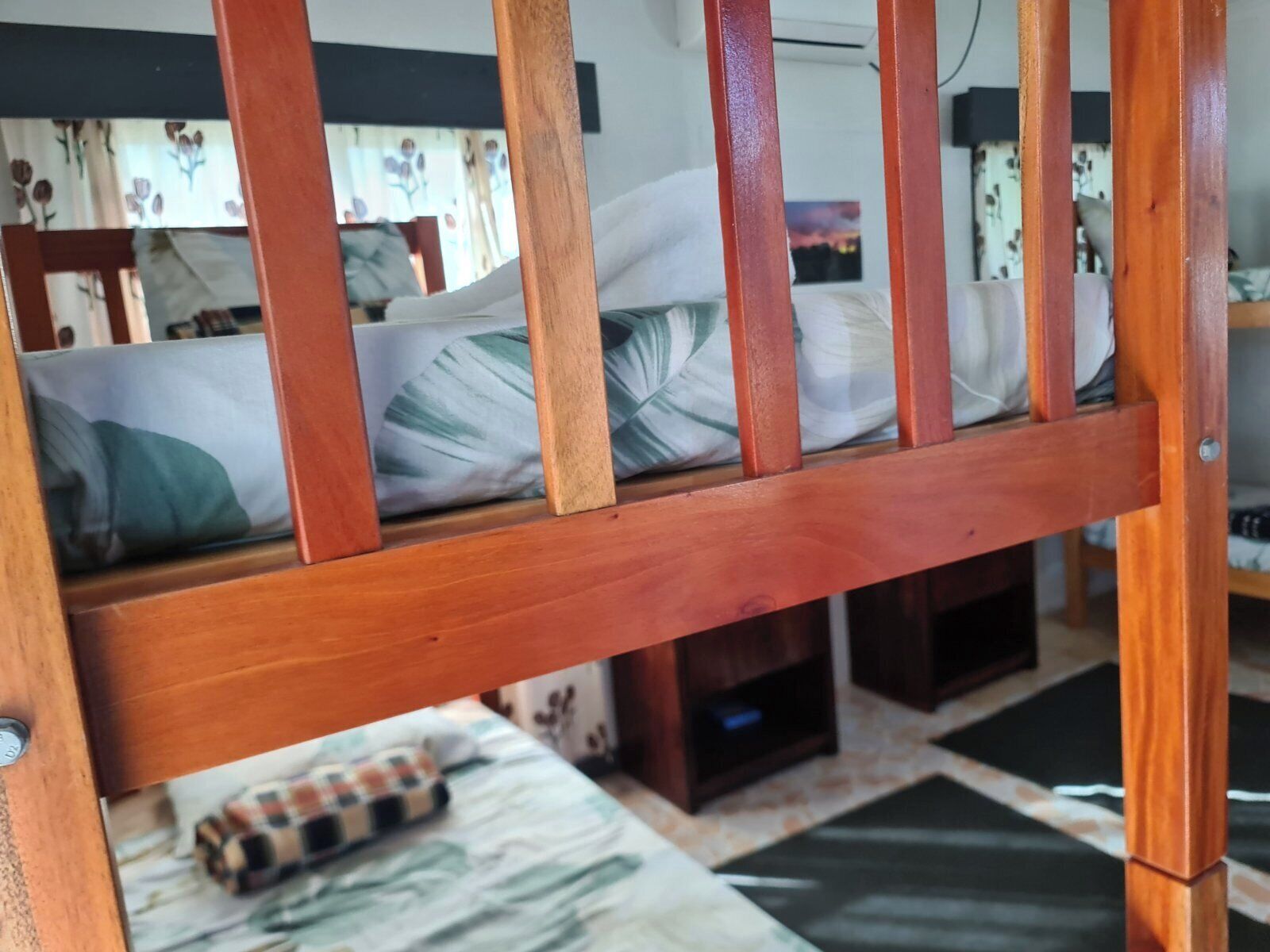 A wooden bunk bed with a mattress and pillows, a small table with a checkered cloth, and a television unit below.