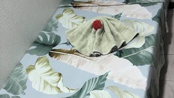 Una cama individual con una colcha estampada, una almohada pequeña y un adorno rojo sobre la cama.