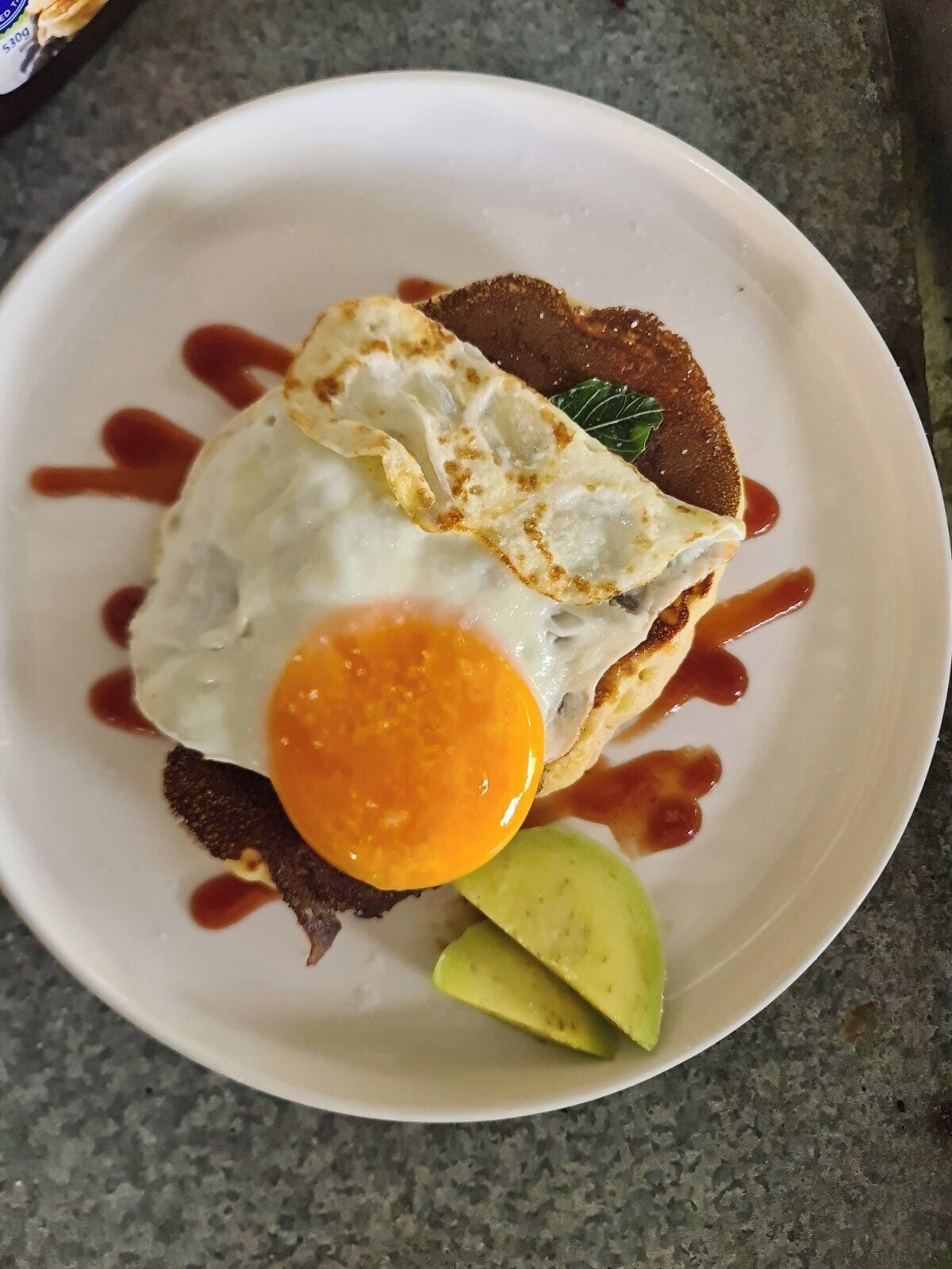 Un plato con un huevo frito, rebanadas de aguacate y una tostada con kétchup.