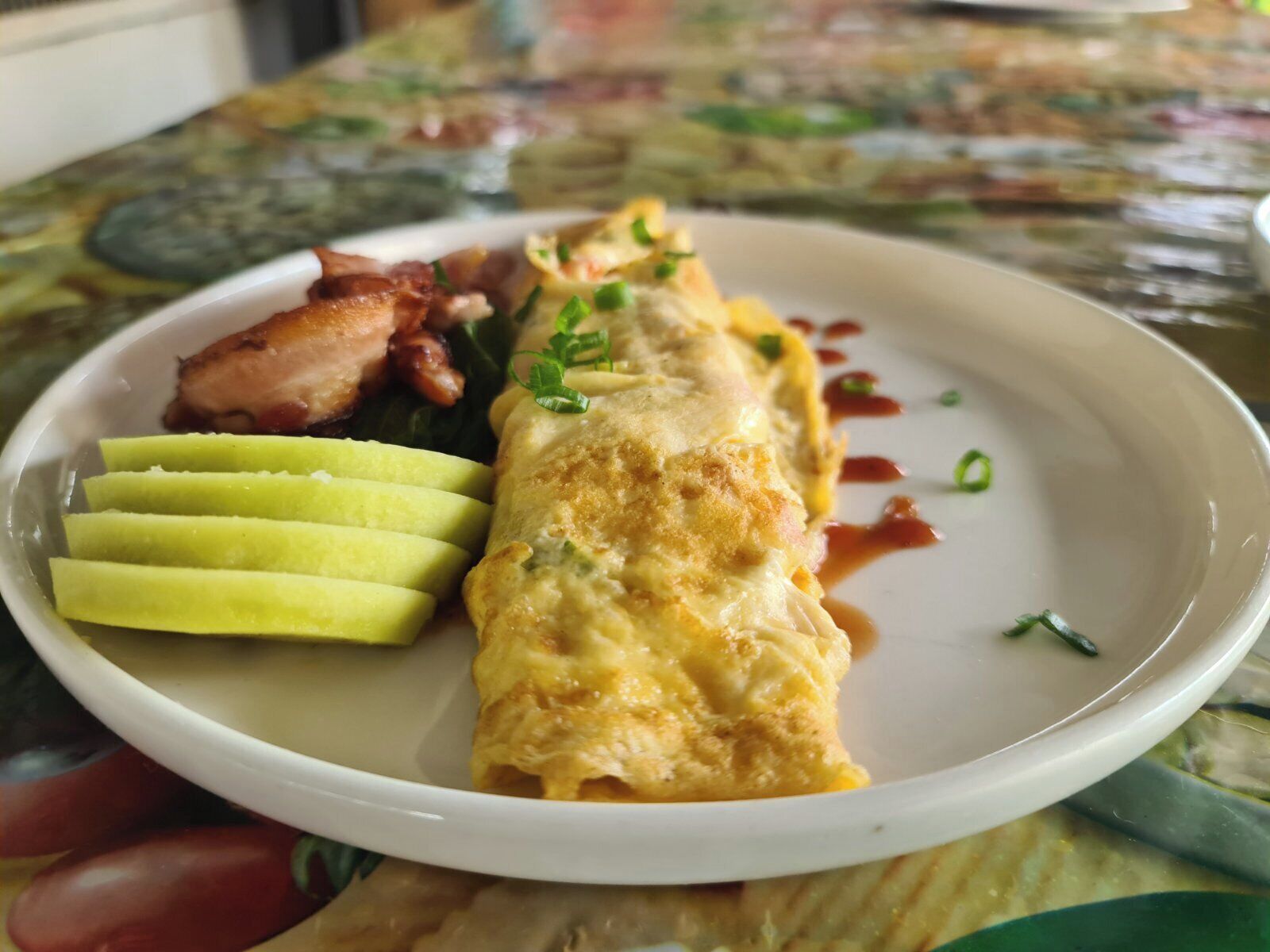 A plate with an omelette, bacon, and sliced avocado.