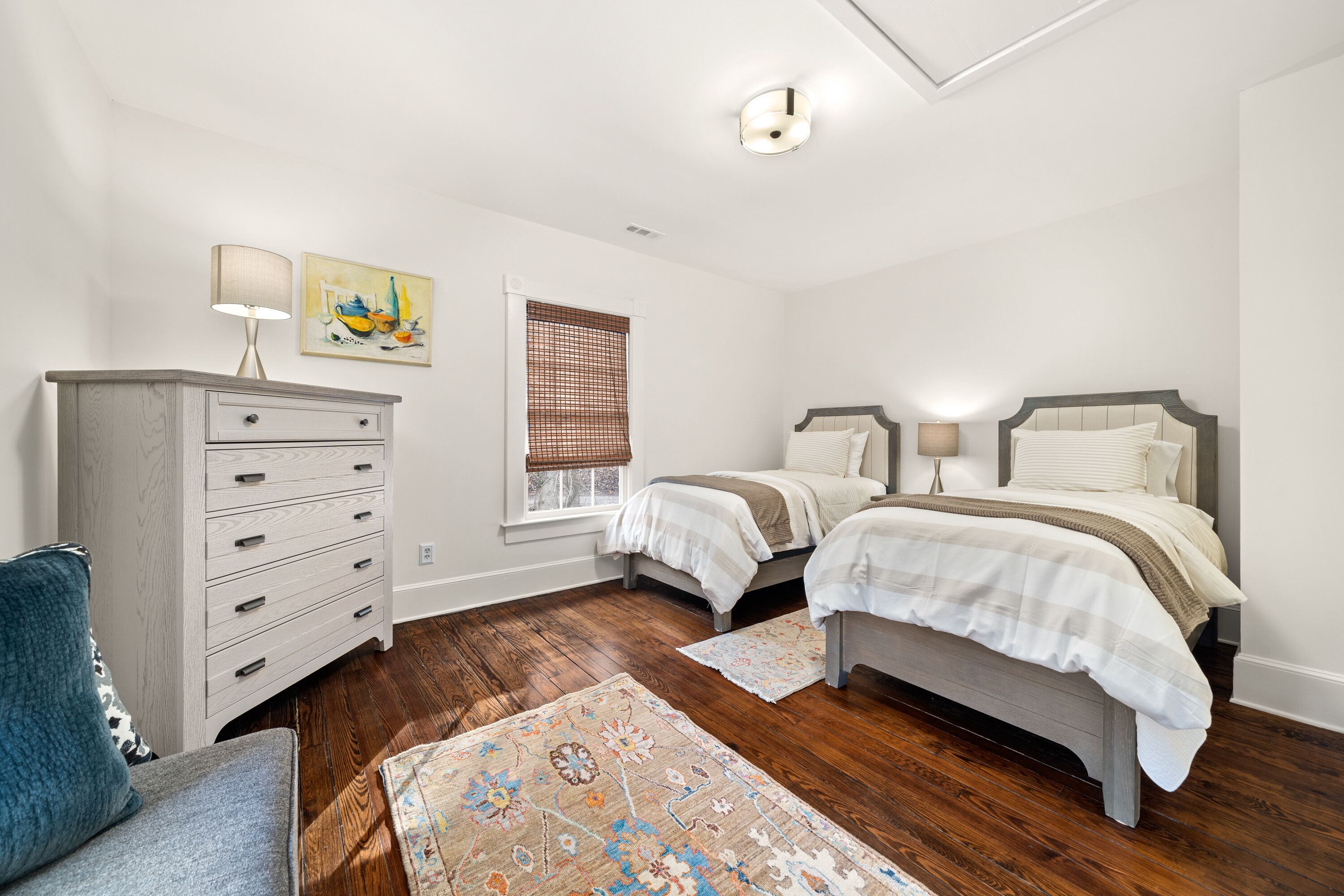 A bedroom with two beds, a dresser, a window with blinds, and a rug.