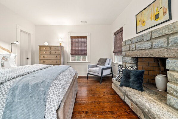 Un dormitorio con cama, cómoda, sillón y chimenea.