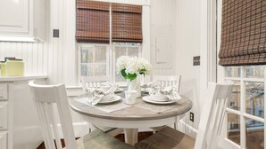 Un comedor con una mesa redonda para cuatro personas, sillas blancas y un jarrón con flores blancas.
