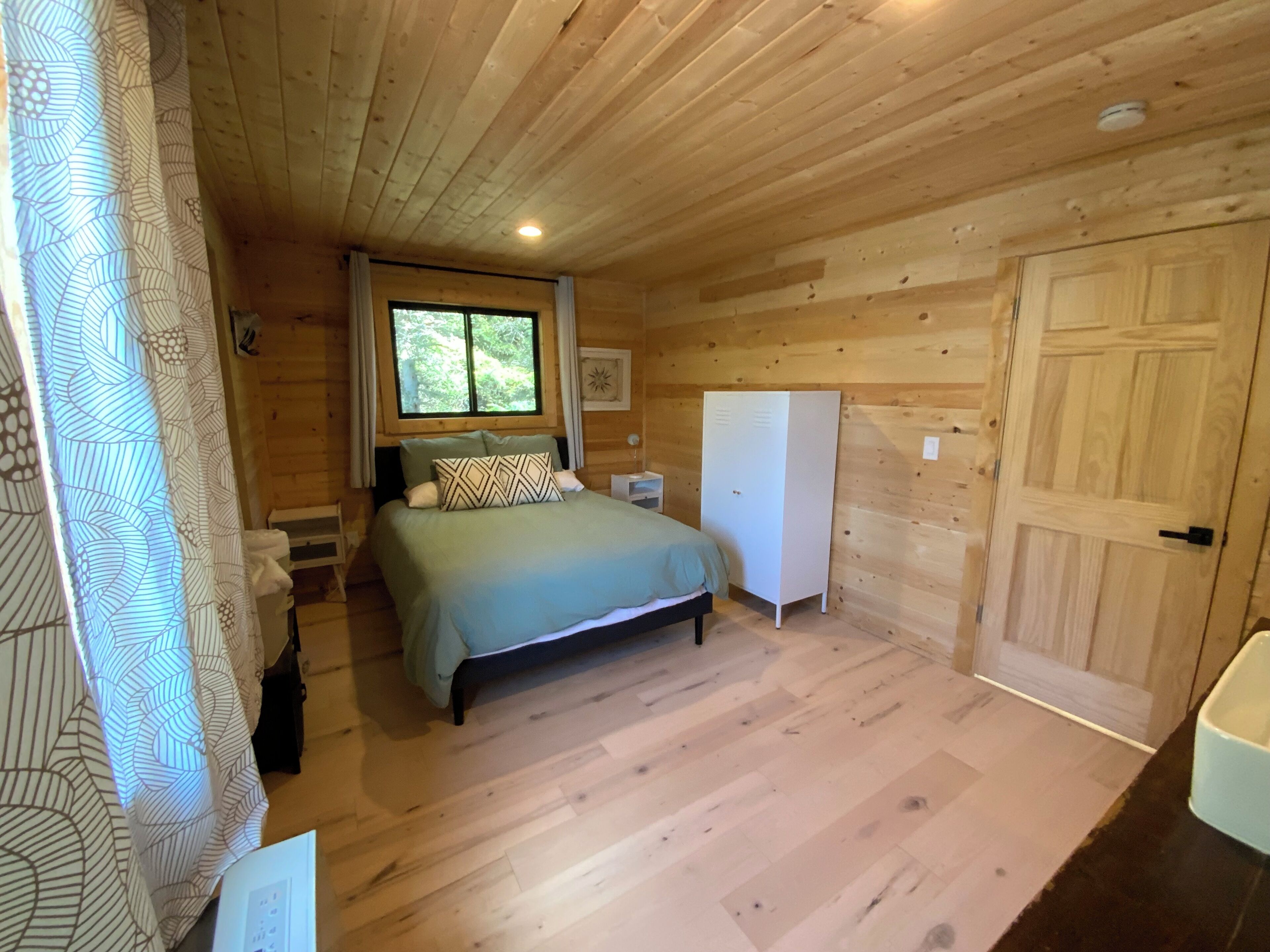 Quarto de cabana de madeira com cama, guarda-roupa e janela.