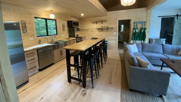 Un'ampia cucina con pareti in legno, un'isola centrale e sgabelli da bar. Nell'area soggiorno, c'è un divano e un tavolo da pranzo.