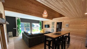 Un accogliente interno in legno con un divano, un tavolo da pranzo con sgabelli e un angolo cottura.