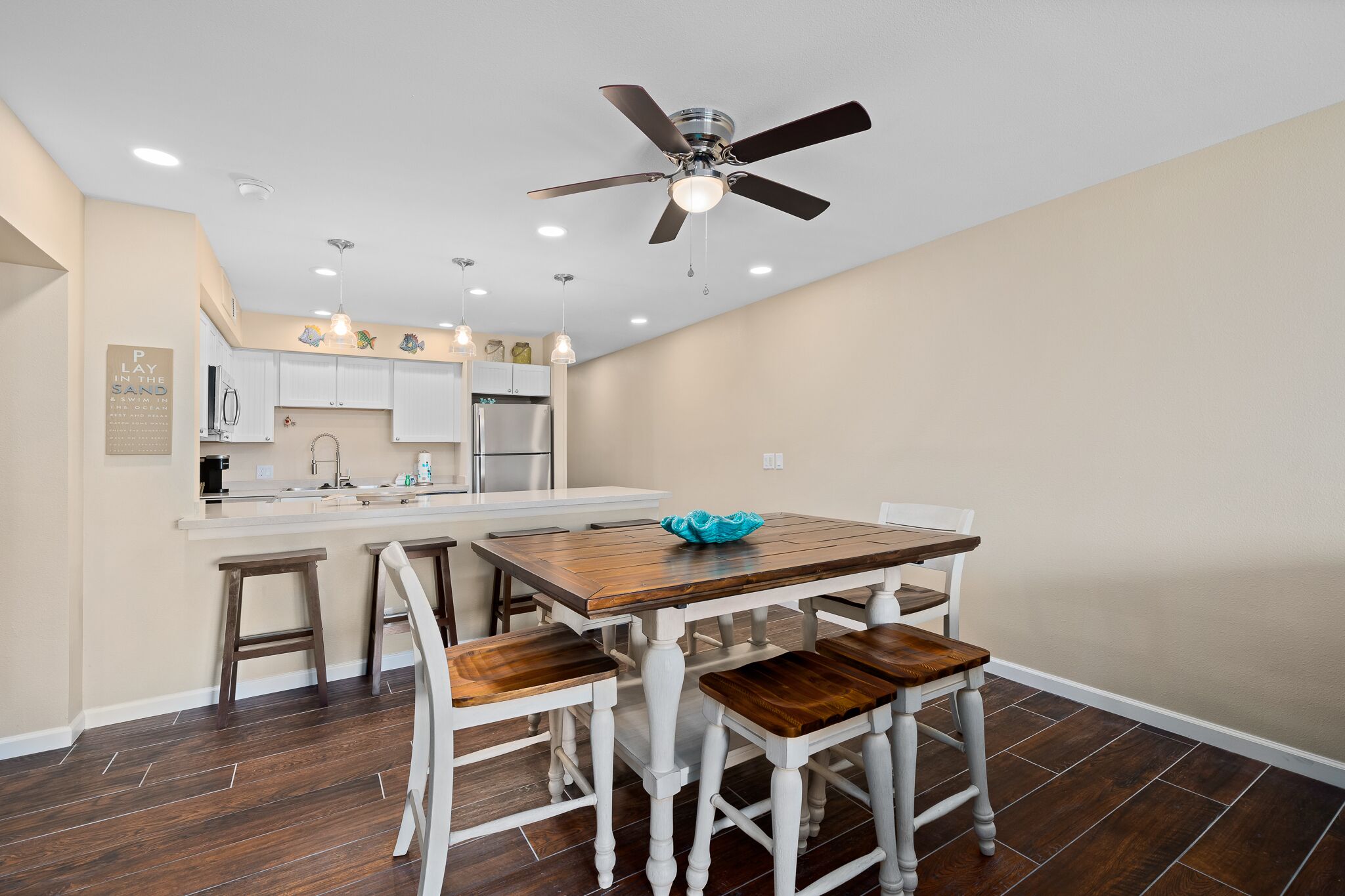 A modern kitchen with white cabinetry, a wooden dining table with four chairs, and a ceiling fan.