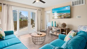 A living room with a ceiling fan, a TV mounted on the wall, and a view of the ocean through the sliding glass doors. - La Mirage Condo 101 Beachfront Condo Resort with Private Boardwalk (Port Aransas)
