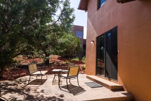 Une terrasse extérieure avec une table et quatre chaises, entourée d’arbres et d’un bâtiment doté d’une grande porte vitrée.