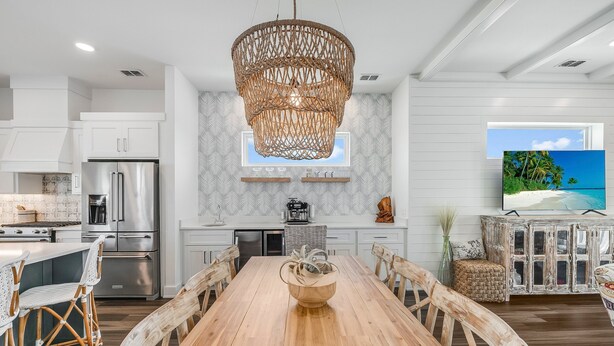 A modern kitchen with a wooden dining table, white cabinetry, and a large woven light fixture. - Private Pool, Golf Cart Included, Boardwalk to Beach (Port Aransas)