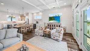 A spacious living area with a sofa, coffee table, and patterned armchairs. A large window offers a view of the outdoors. - Private Pool, Golf Cart Included, Boardwalk to Beach (Port Aransas)