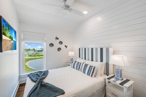 A bedroom with a bed, a nightstand, a lamp, a window with a view of a beach, and a ceiling fan. - Private Pool, Golf Cart Included, Boardwalk to Beach (Port Aransas)