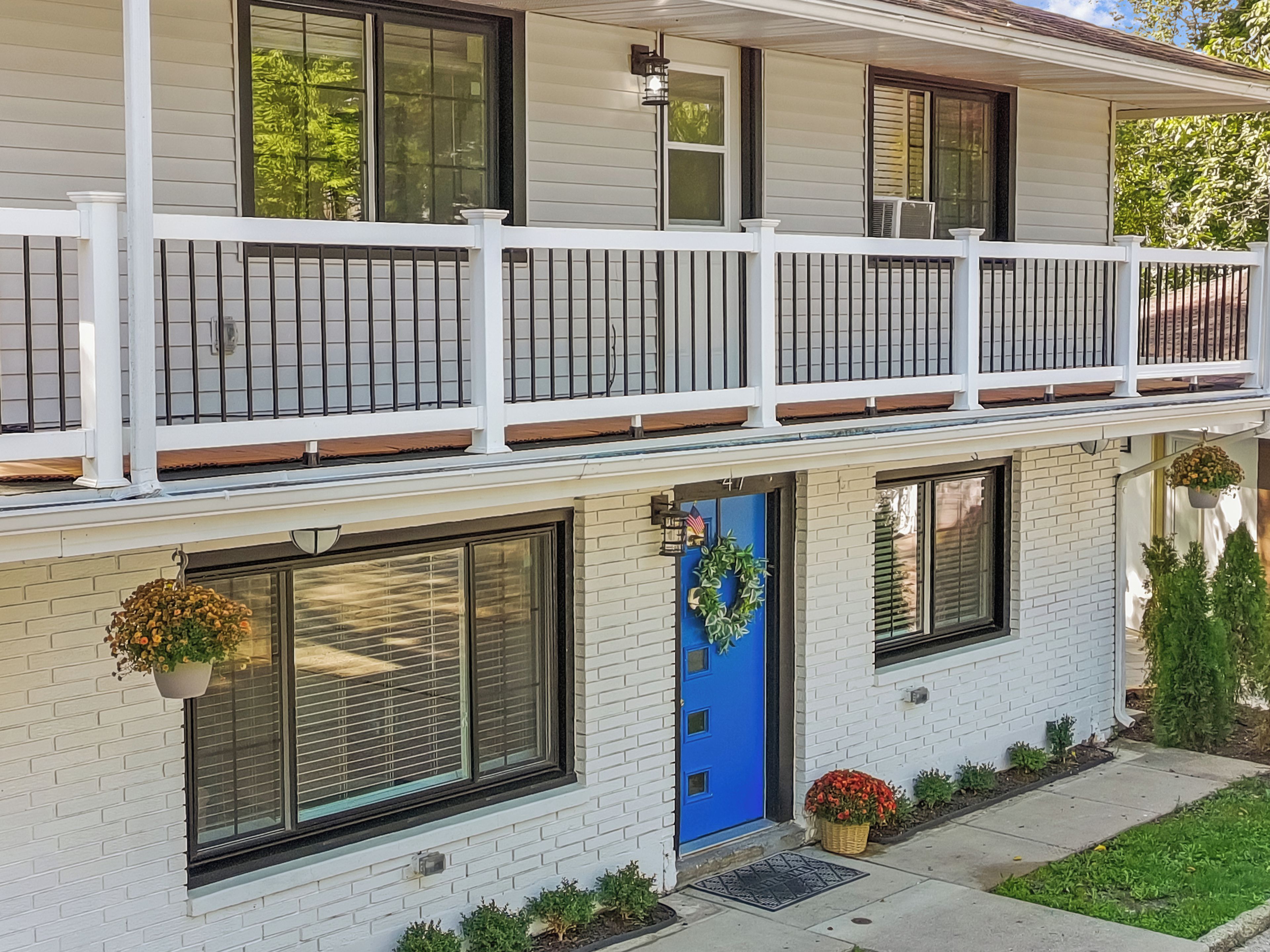 Une maison à deux étages avec une porte d’entrée bleue, des balustrades blanches et une façade en briques.