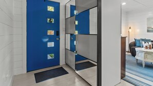Un hall d’hôtel moderne avec une porte bleue, une cloison en verre et un espace détente comprenant une table blanche et des coussins bleus.
