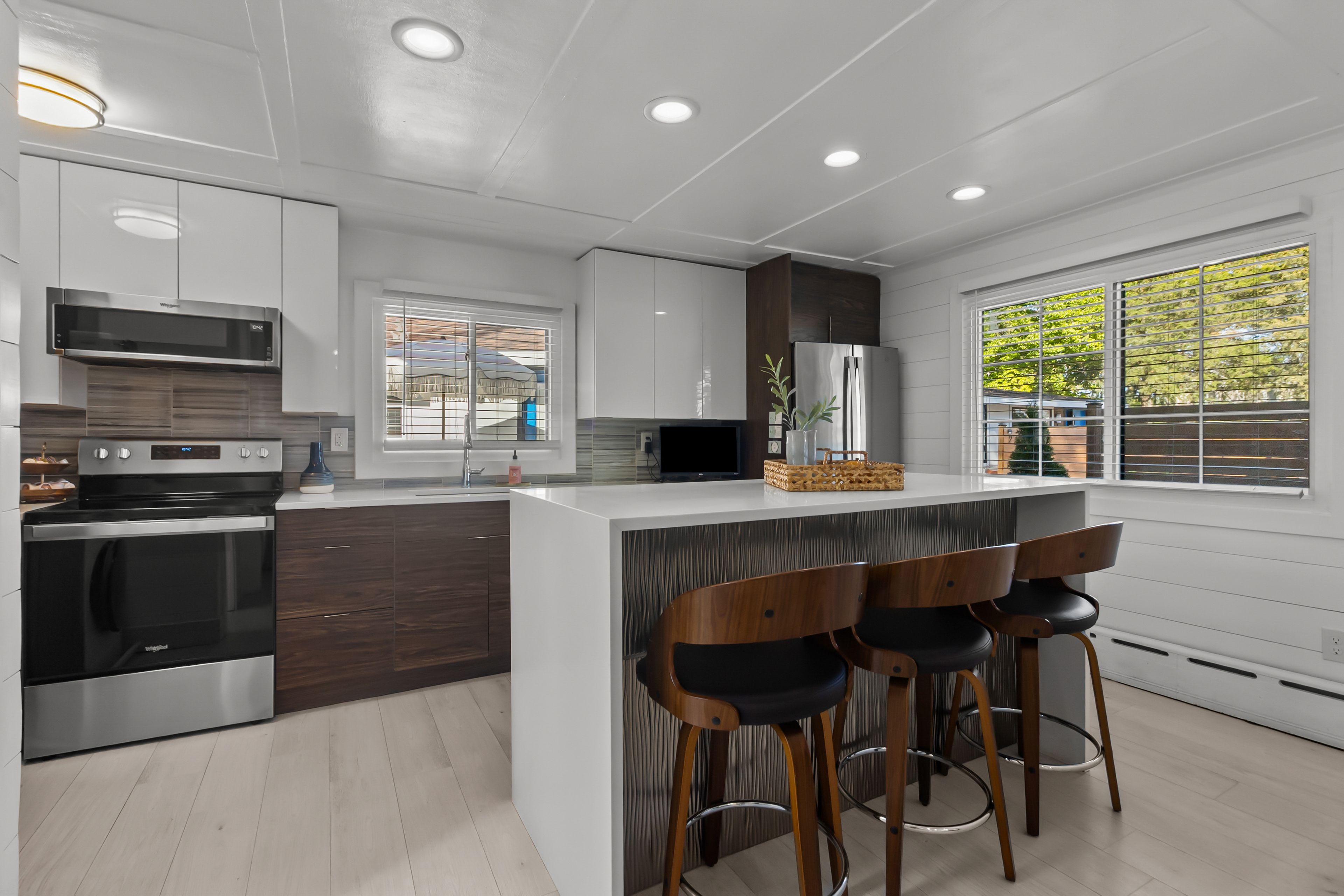 A modern kitchen with a central island, bar stools, and a large window.
