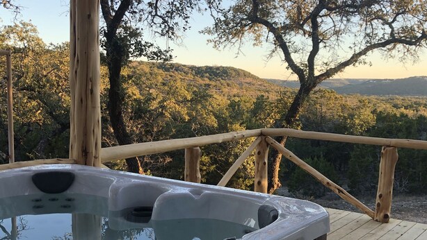 Un jacuzzi en una terraza de madera con vistas a árboles y colinas.