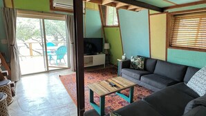 Amplia sala de estar con un sofá grande, una mesa de centro de madera y una televisión. Hay una puerta corredera de vidrio que da a un patio al aire libre.