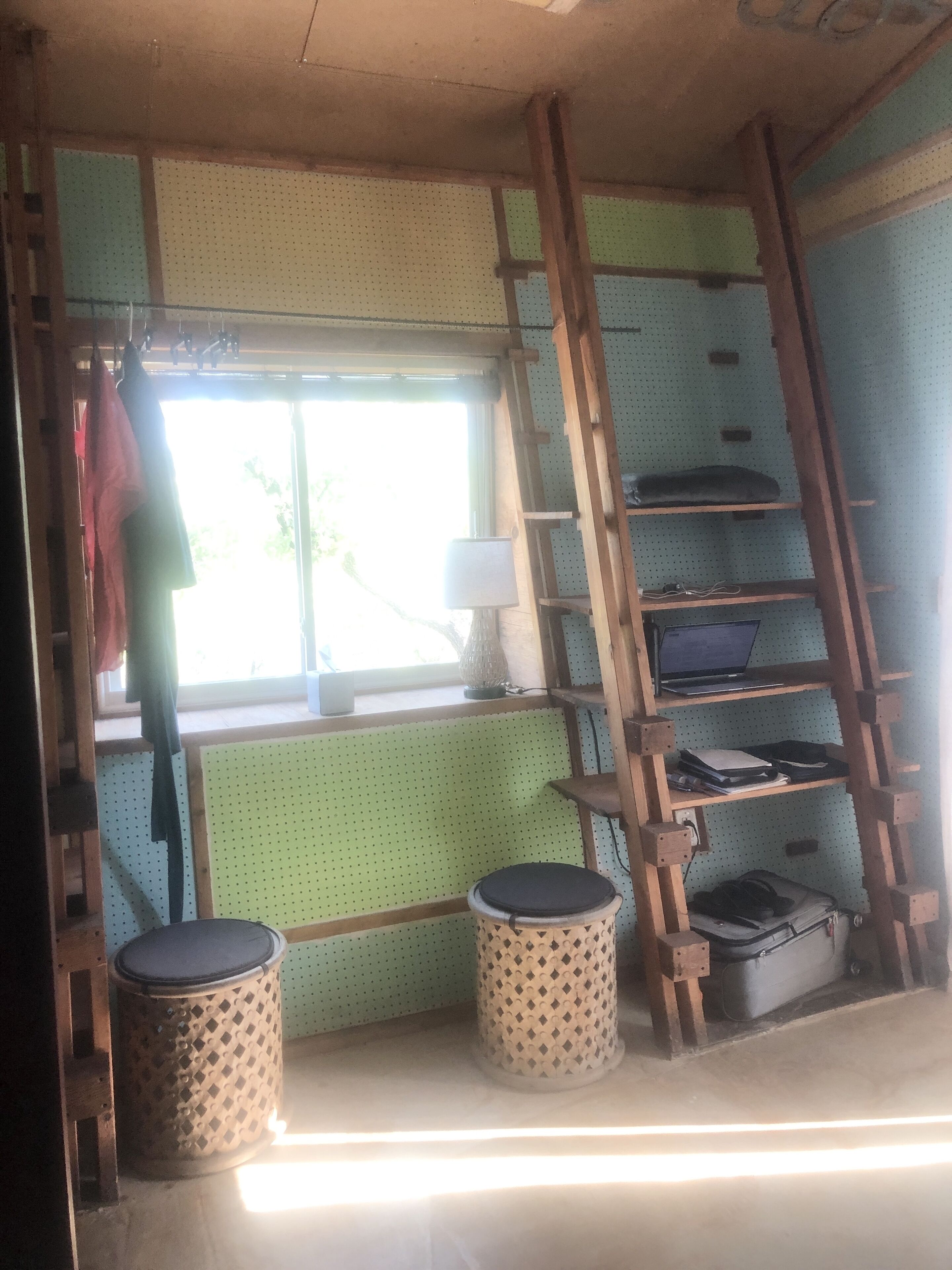 Una habitación con ventana, una escalera de madera, estanterías y dos taburetes redondos.