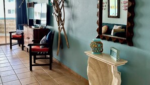 Una habitación con pared azul, una silla de madera, un sofá, un espejo decorativo y una pequeña mesa con un jarrón.