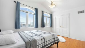 A bedroom with a bed, two windows with curtains, a door, and a ceiling light.