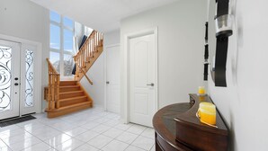 A spacious room with a wooden staircase, white tiled floor, and a door with decorative glass panels.