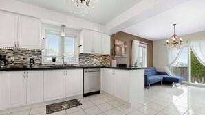 A modern kitchen with white cabinets, a black countertop, and a tiled backsplash. There is a blue sofa in the adjacent living area.