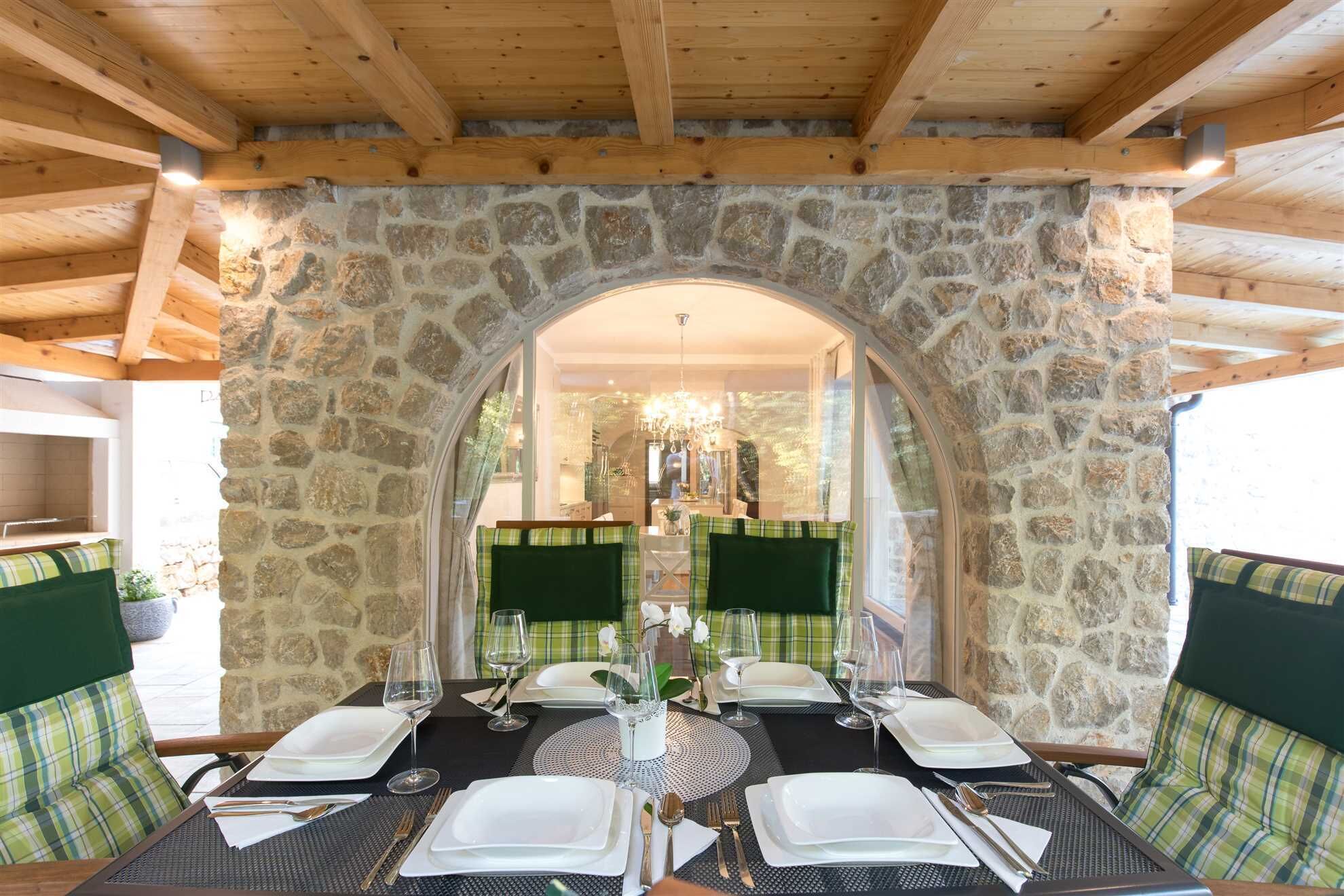 Un espace repas avec des murs en pierre, des poutres en bois et des chaises recouvertes d’un tissu vert.