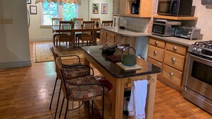 A kitchen with wooden cabinets, a central island, bar stools, a microwave, a toaster, and a stove. - Cozy farmhouse with jacuzzi 10 min from Lansing, NC and Grayson Highlands (Lansing)