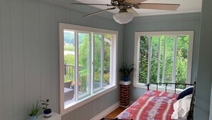 A bedroom with a bed, two windows, a ceiling fan, and a brick fireplace. - Cozy farmhouse with jacuzzi 10 min from Lansing, NC and Grayson Highlands (Lansing)