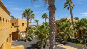 A courtyard with palm trees, yellow buildings, and a clear blue sky. - Cueva Azul Corralejo by iRent Fuerteventura (Corralejo)