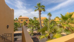 A courtyard with palm trees and buildings with yellow facades. - Cueva Azul Corralejo by iRent Fuerteventura (Corralejo)