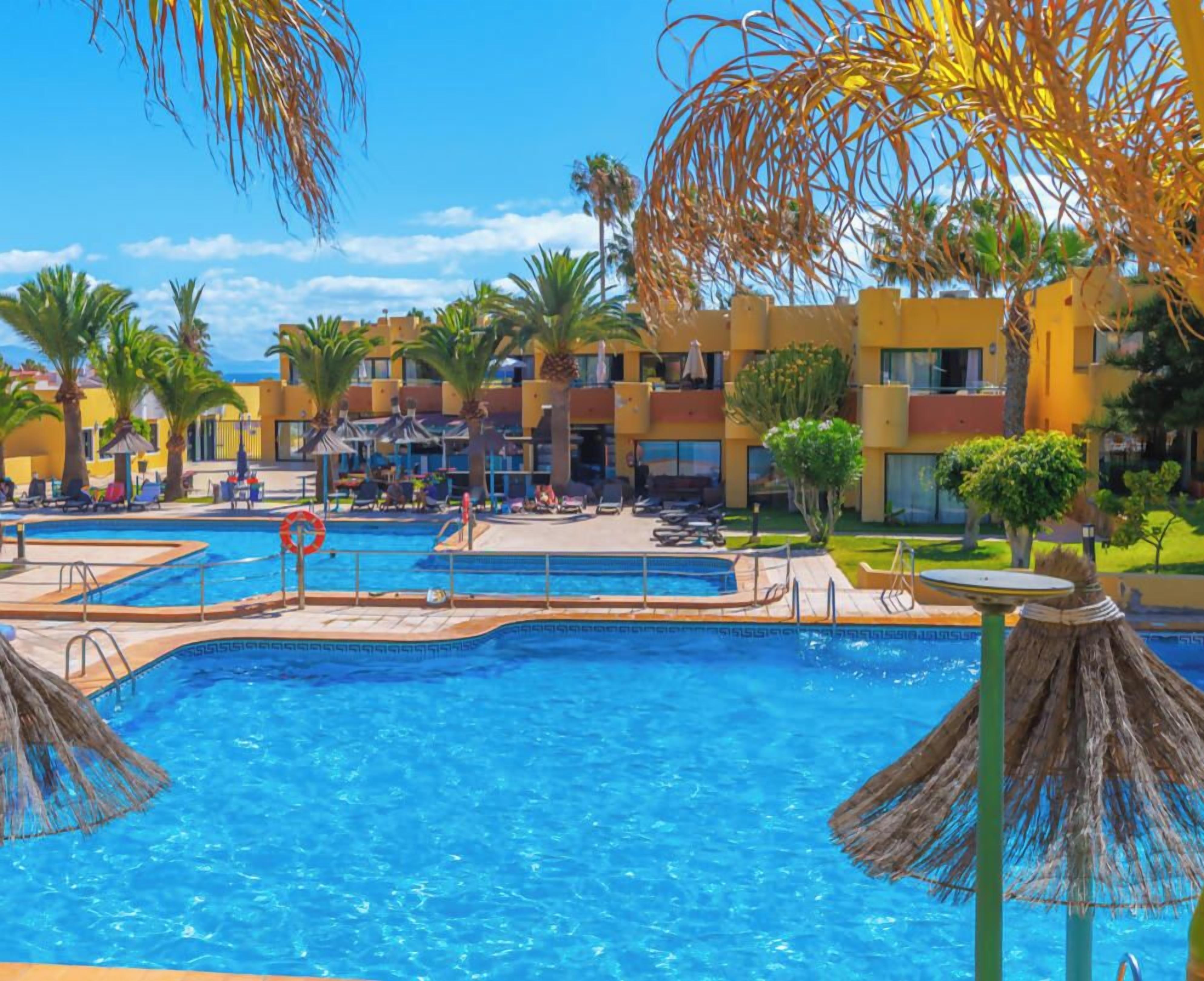 A hotel pool area with multiple swimming pools, lounge chairs, and palm trees.