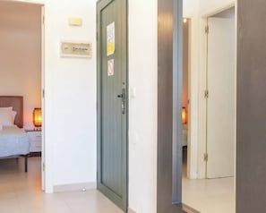 Una habitación de hotel con cama, mesita de noche, lámpara y una puerta que da a otra estancia.