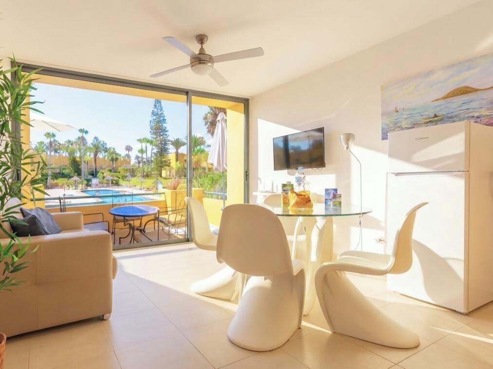 A modern living room with a glass door leading to a pool area, a flat-screen TV, and a refrigerator.