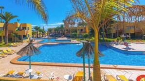 A resort pool area with multiple pools, sun loungers, and palm trees.