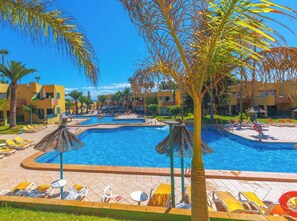 Zona de piscina en un resort, con varias piscinas, tumbonas y palmeras.