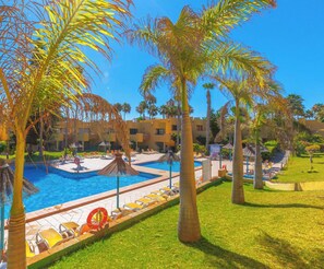 Una piscina con sillas de descanso, palmeras y un edificio al fondo.