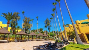 A resort pool area with sun loungers, palm trees, and a clear blue sky.