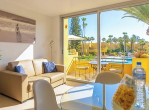 A modern living room with a sofa, a glass table, and a view of a pool and palm trees. - Palmira Sea View and Lobos Island Corralejo (Corralejo)