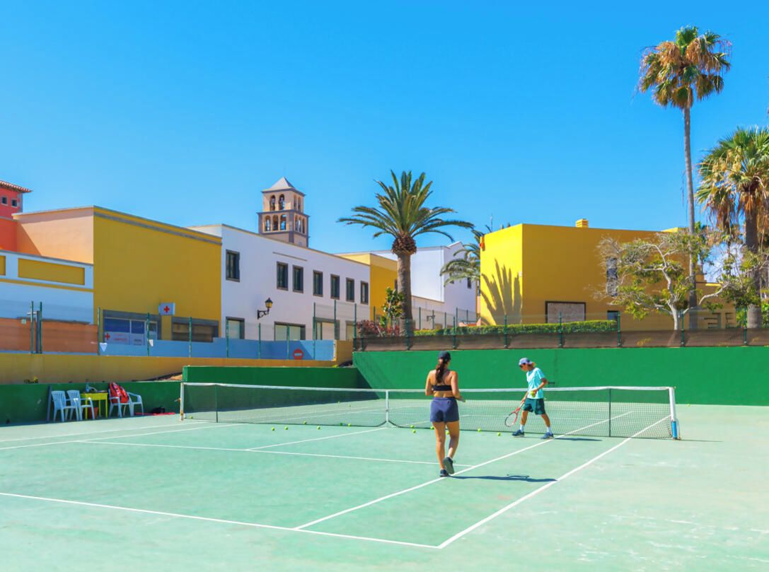 Una cancha de tenis con red, rodeada de edificios y palmeras.