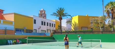A tennis court with a net, surrounded by buildings and palm trees.