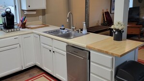 Una cucina moderna con mobili bianchi, una lavastoviglie in acciaio inossidabile e un piano di lavoro in legno.