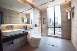 Een moderne badkamer met een groot raam, een douchecabine van glas en een wit toilet.