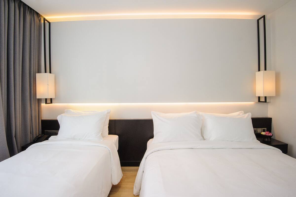 Une chambre d’hôtel avec deux lits, une tête de lit sombre et un luminaire fixé au mur.