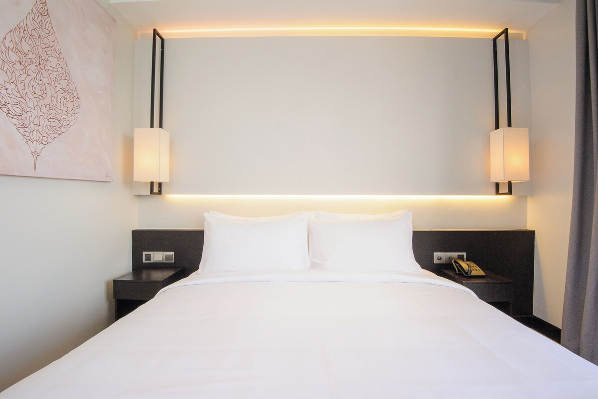 A hotel room with a large bed, two bedside tables, a nightstand with a phone, and two wall-mounted lamps.